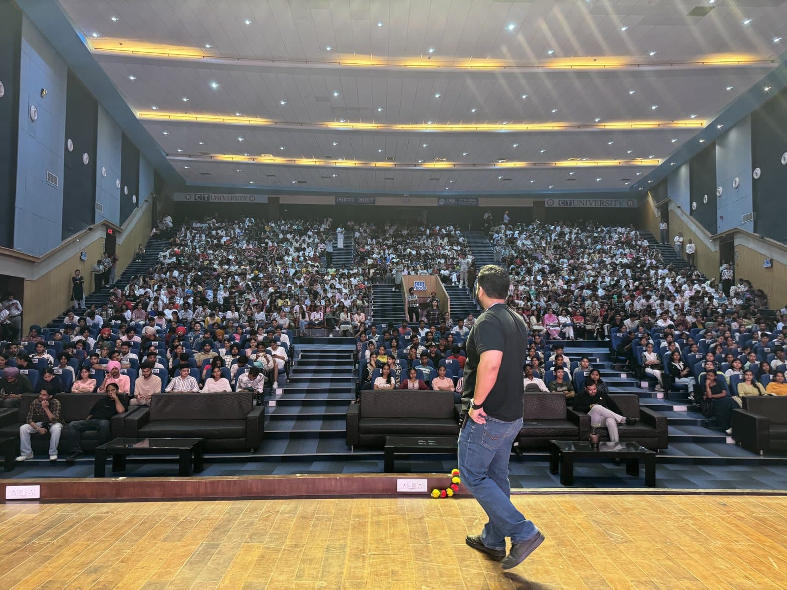 Gourav Gupta walking across the stage in front of a packed auditorium